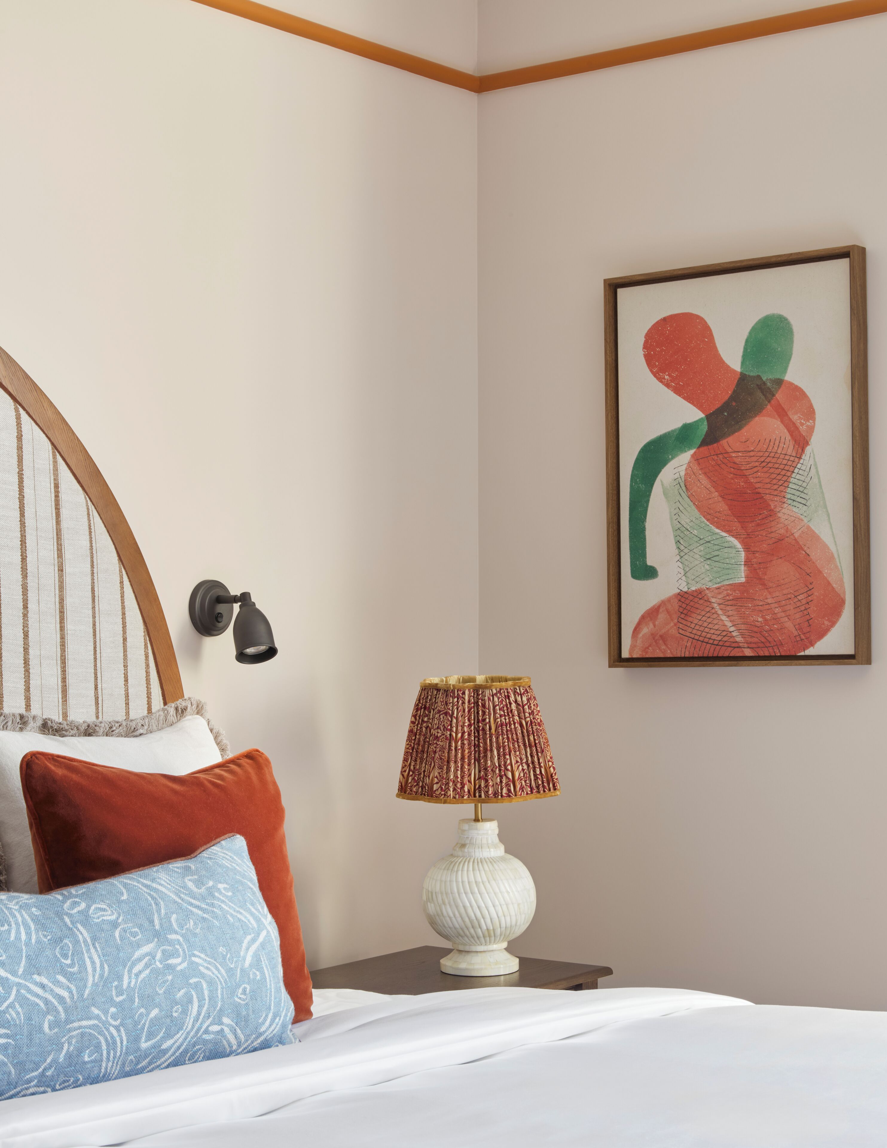 A bedroom with a bed, pillows, a lamp, a wall-mounted artwork, and a nightstand.