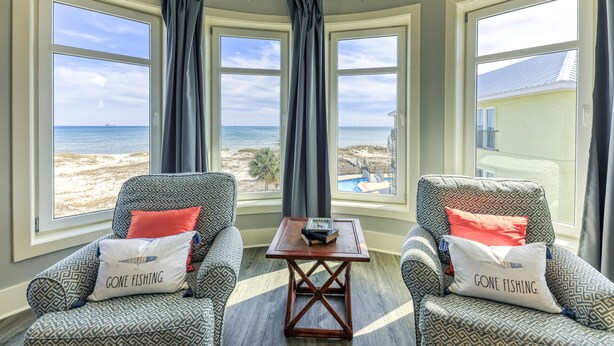 A corner room with two patterned armchairs, a small wooden table, and large windows offering a view of the beach and ocean. - Oyster House B2 - Sleeps 20 - Beachfront w/ Pool (Gulf Shores)