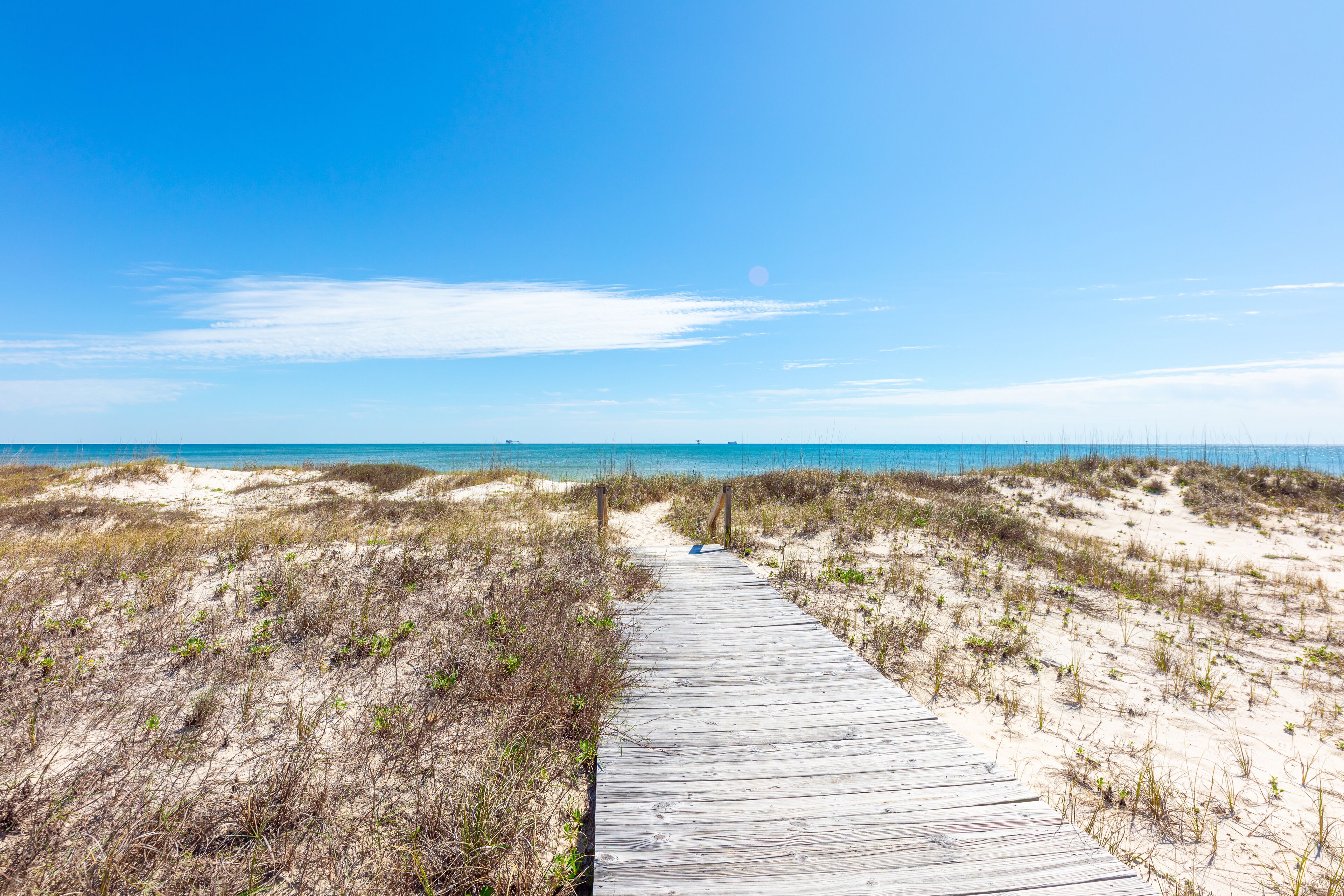 A wooden boardwalk leading to a beach with clear skies and distant ocean views.