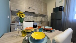Une cuisine moderne avec des meubles en bois, une cuisinière à gaz, un réfrigérateur et une table à manger agrémentée de bols et de verres colorés.