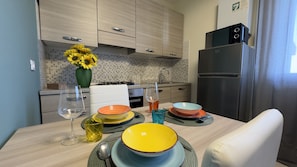 A modern kitchen with light wood cabinets, a black refrigerator, and a dining table set with colorful bowls and glasses.