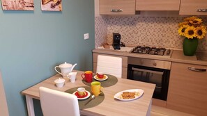 A small kitchen with a dining table, a coffee maker, a stove, and a vase with sunflowers.