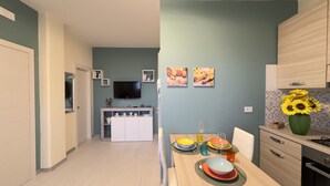Une cuisine moderne avec un coin repas, un téléviseur à écran plat fixé au-dessus du comptoir et un vase rempli de tournesols sur la table.