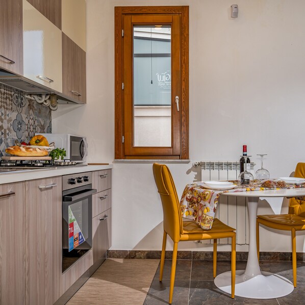 A compact kitchen with a dining area, featuring a stove, oven, microwave, and a dining table with chairs. - Casa del Golfo Cascio 3 Secondo Piano (Castellammare del Golfo)