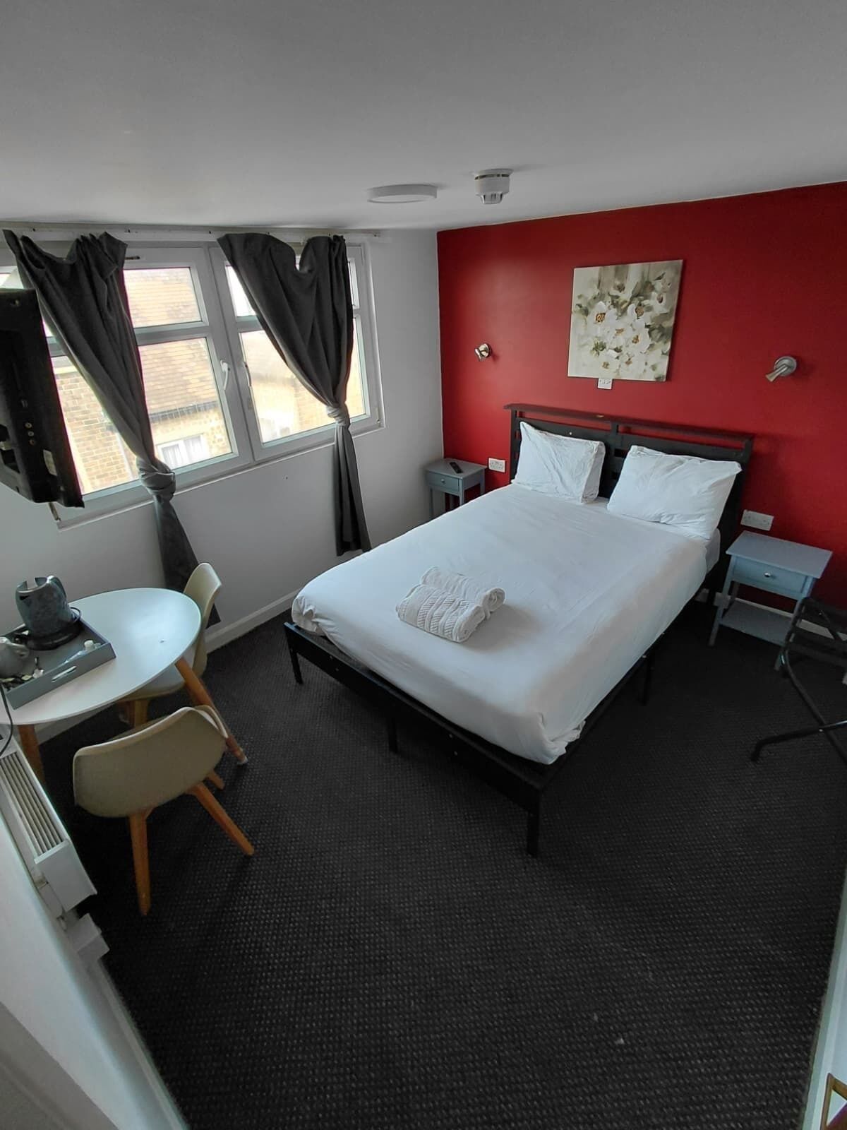 Una camera d'albergo con un letto, una scrivania, una sedia, un tavolino, un comodino e una finestra con tende.
