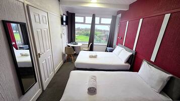 A hotel room with two beds, a desk, a chair, a mirror, and a window with a view of greenery.