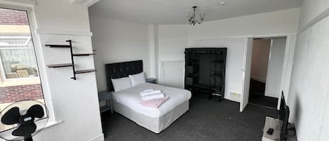 A modern bedroom with a large bed, a wardrobe, a desk with a computer, and a fan.