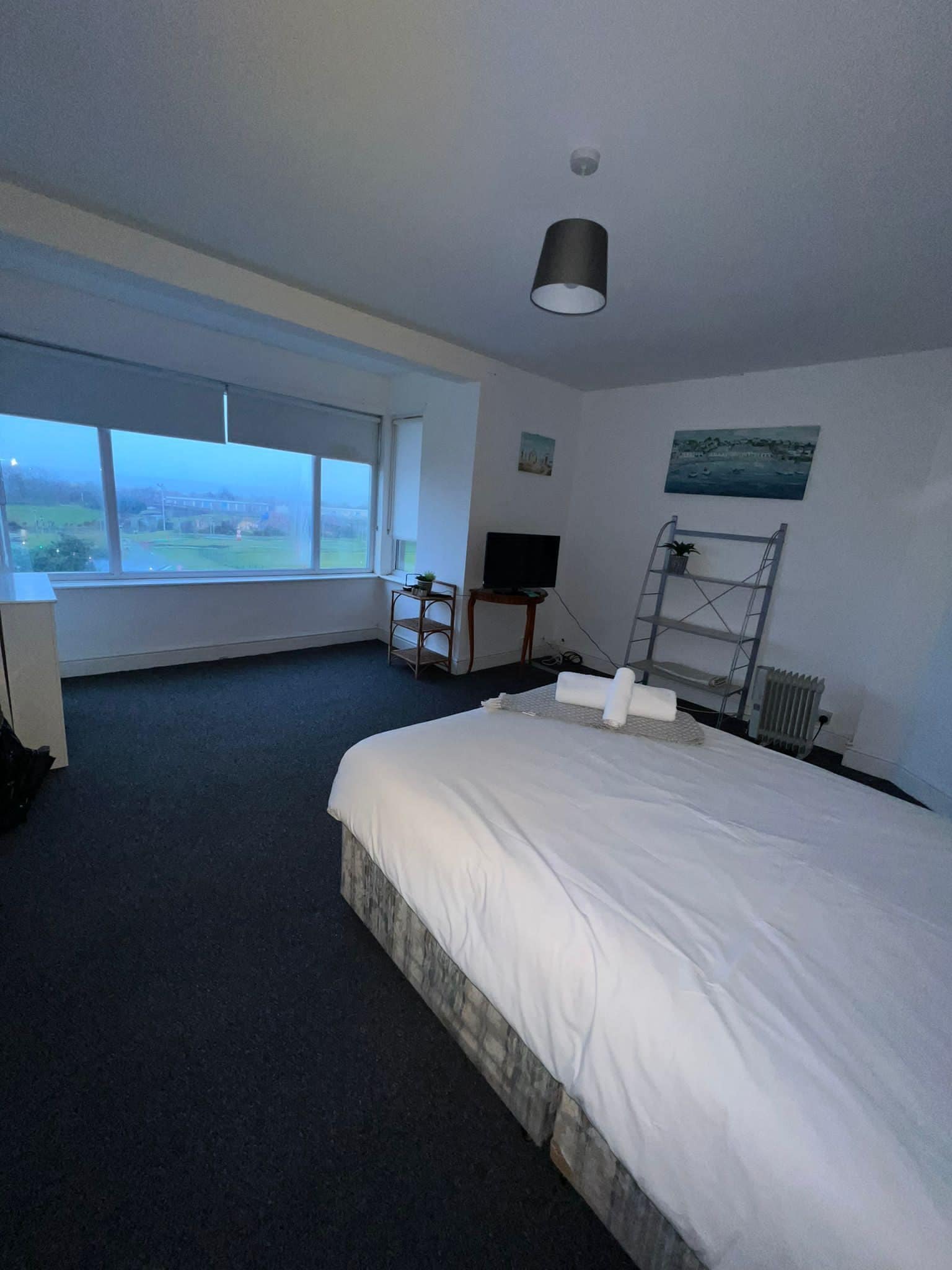 A hotel room with a large bed, a TV, a desk, and a window with a view of the countryside.