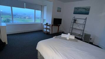 A hotel room with a large bed, a TV, a desk, and a window with a view of the countryside.