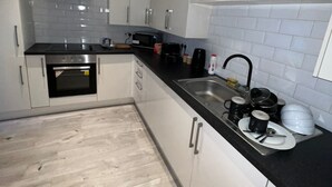 A modern kitchen with white cabinets, a black countertop, and a stainless steel range hood. - Harbour Stays (Skegness)