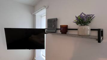 A wall-mounted shelf with a flat-screen TV, a decorative plaque, a candle, and a potted plant.