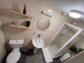 A bathroom with a toilet, bidet, and a glass-enclosed shower. There are shelves with decorative items and a mirror on the wall. - Harbour Stays (Skegness)