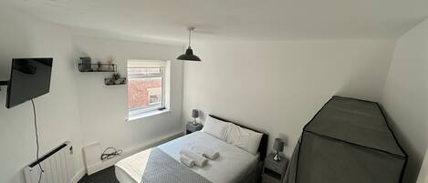 A bedroom with a bed, bedside tables, a TV, a window, and a radiator.