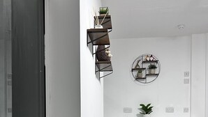 A modern dining area with a round table and six chairs, a potted plant on the windowsill, and wall-mounted shelves with decorative items. - Harbour Stays (Skegness)