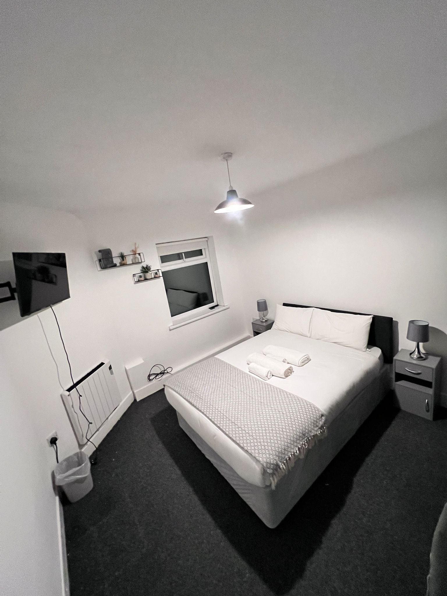 A modern bedroom with a large bed, bedside tables, a window, and a ceiling light.