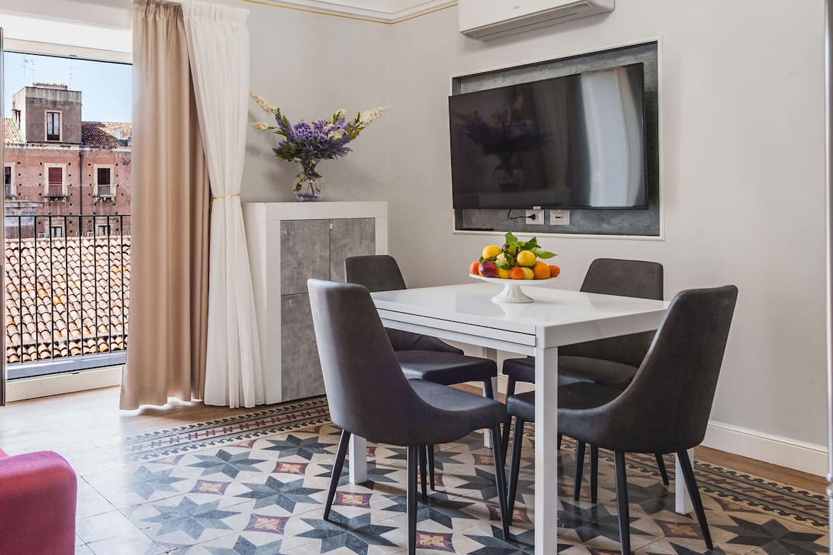 A modern dining area with a white table and black chairs, a vase with flowers, and a fruit bowl.