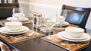 Een eettafel gedekt met witte borden, kommen en glazen wijn, met zilveren zout- en peperstel en een decoratief boek.