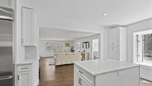 A modern kitchen with white cabinetry, a marble island, and hardwood flooring. - New Hamptons House in Sag harbor + Pool + 8 bedroom (Sag Harbor)