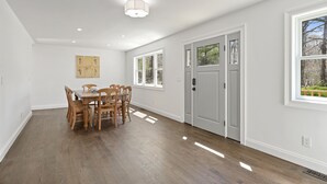 A spacious room with hardwood flooring, a dining table with chairs, large windows, and a door with a view of greenery outside. - New Hamptons House in Sag harbor + Pool + 8 bedroom (Sag Harbor)