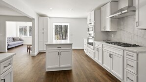 A modern kitchen with white cabinetry, a central island, and a view of a forest through a large window. - New Hamptons House in Sag harbor + Pool + 8 bedroom (Sag Harbor)