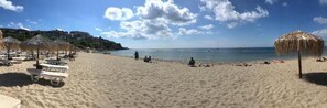 Relax on the beach with comfortable sun loungers and umbrellas, surrounded by a scenic hill in the background.