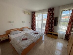 Two single beds with white bedding, a flat-screen TV, and a large window with an outdoor view.