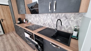 A modern kitchen with a black countertop, a sink, and a dishwasher. - Résidence Cosy et Moderne (Morvillars)