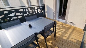 A balcony with a wooden floor, a metal railing, and a table with chairs. - Résidence Cosy et Moderne (Morvillars)