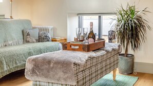 Ein gemütliches Wohnzimmer mit einer Couch, einer Bank, einer Topfpflanze und einem Tablett mit einer Flasche und Gläsern.