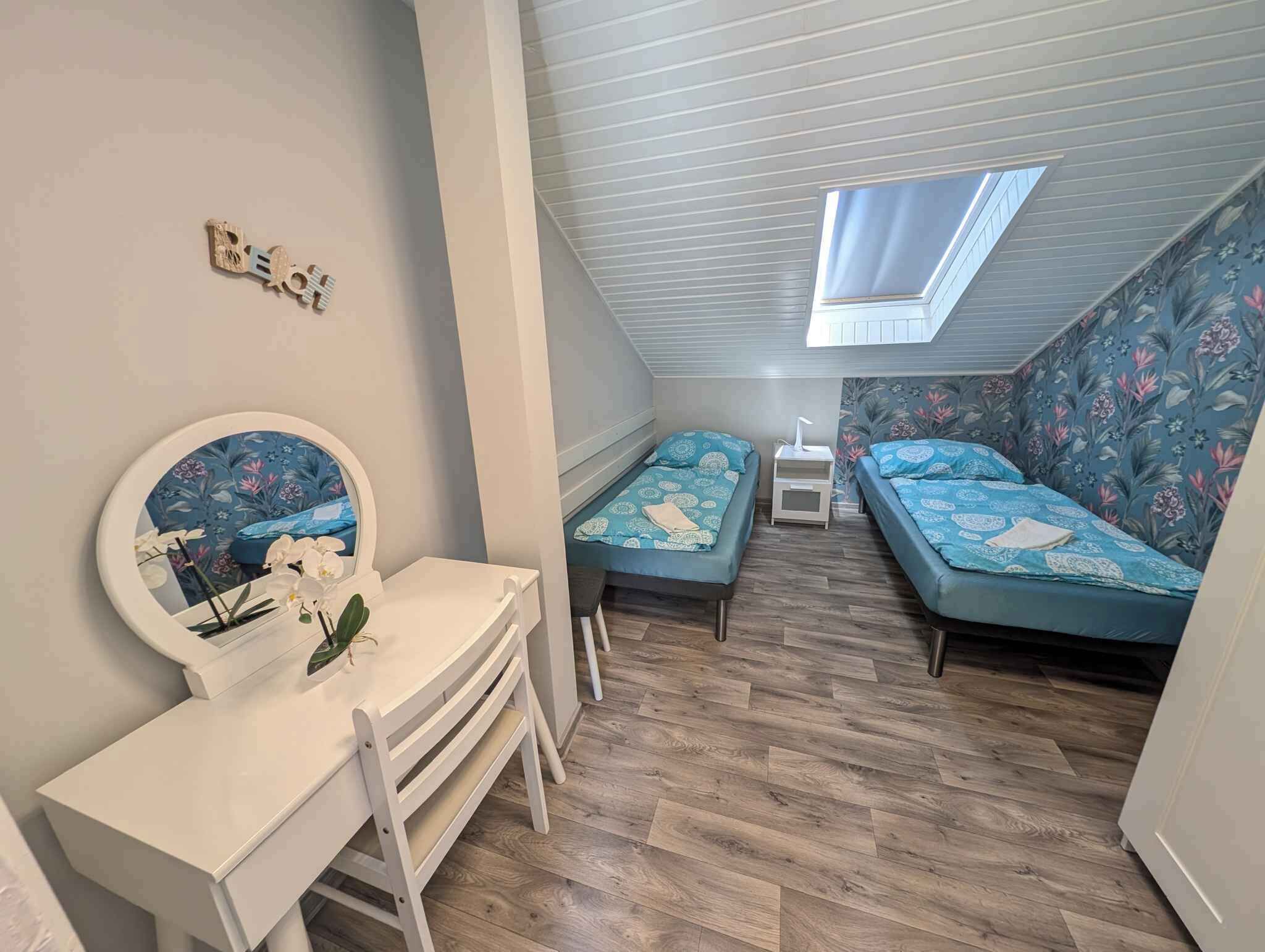 Ein kleines Schlafzimmer mit zwei Einzelbetten, einem kleinen Schreibtisch mit Spiegel und einem Oberlicht.