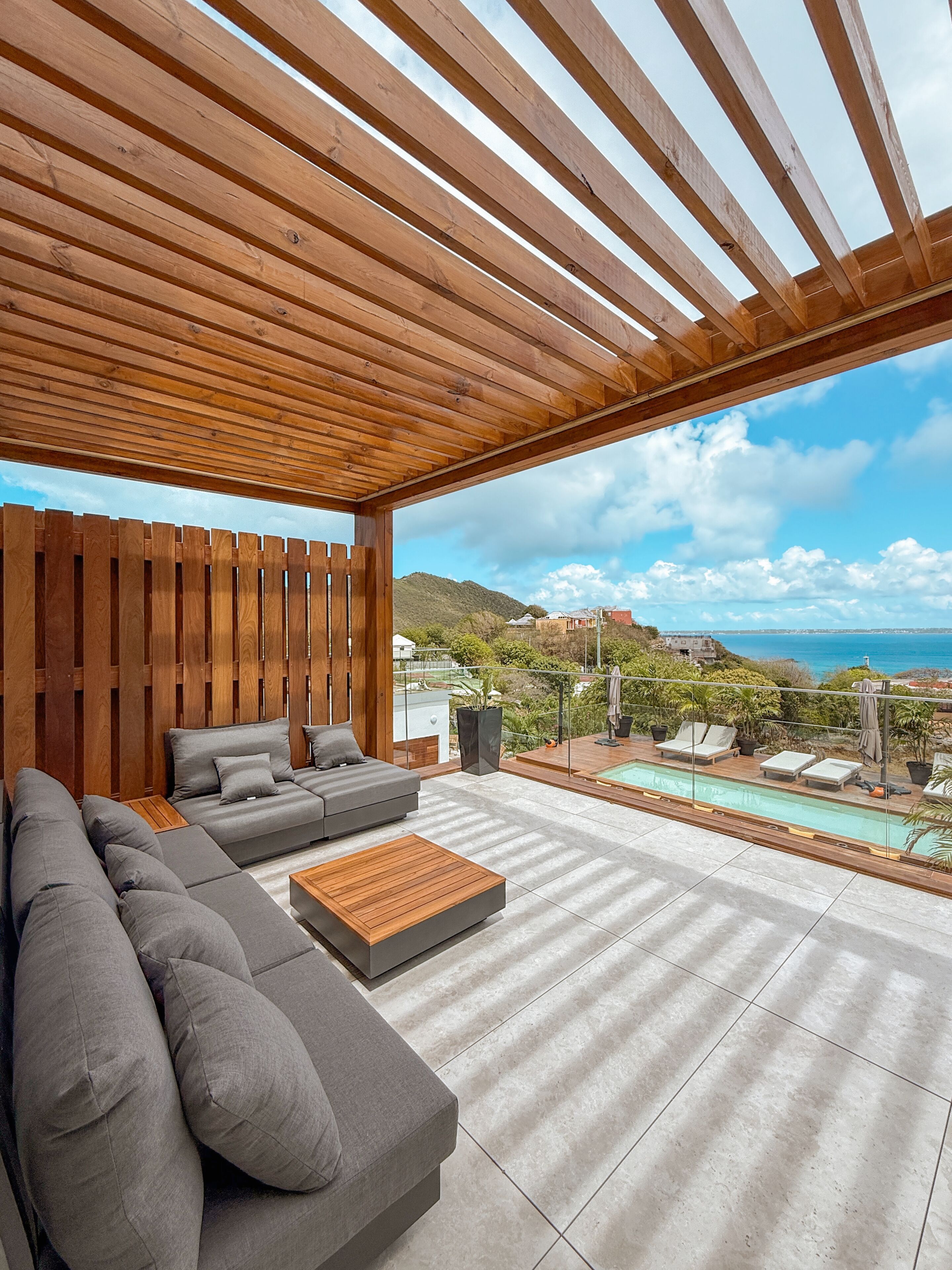 Ein moderner Außenbereich mit einer Holz-Pergola, einem grauen Sofa, einem Holztisch und einem Pool.