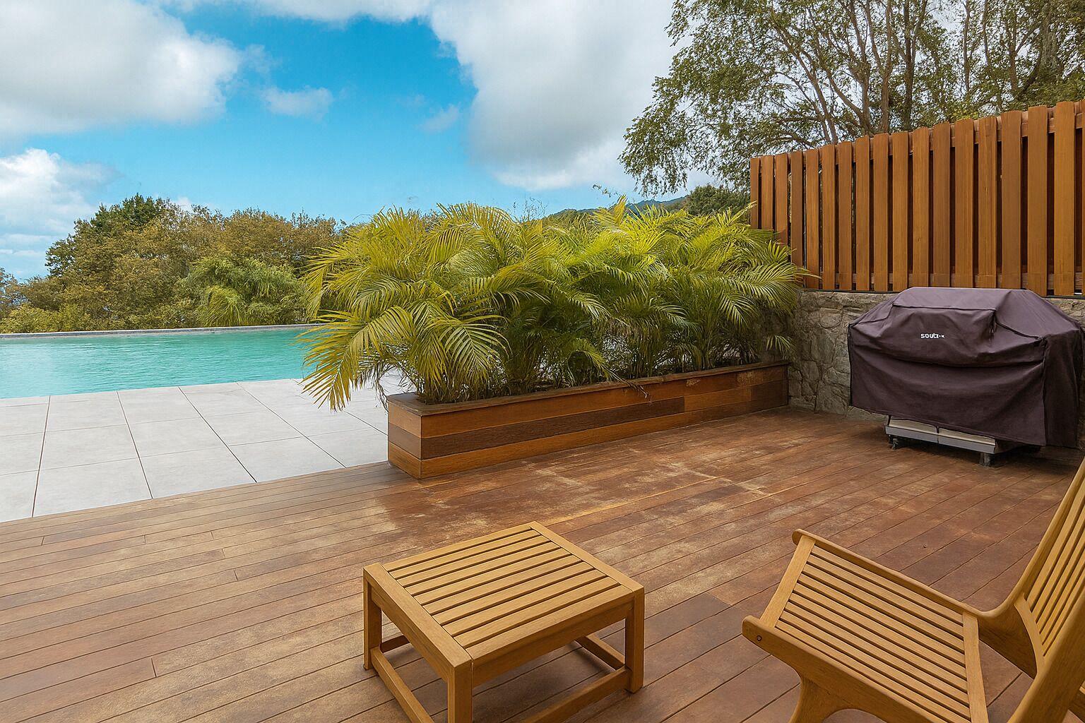 A wooden deck with a pool, outdoor seating, and a barbecue grill.