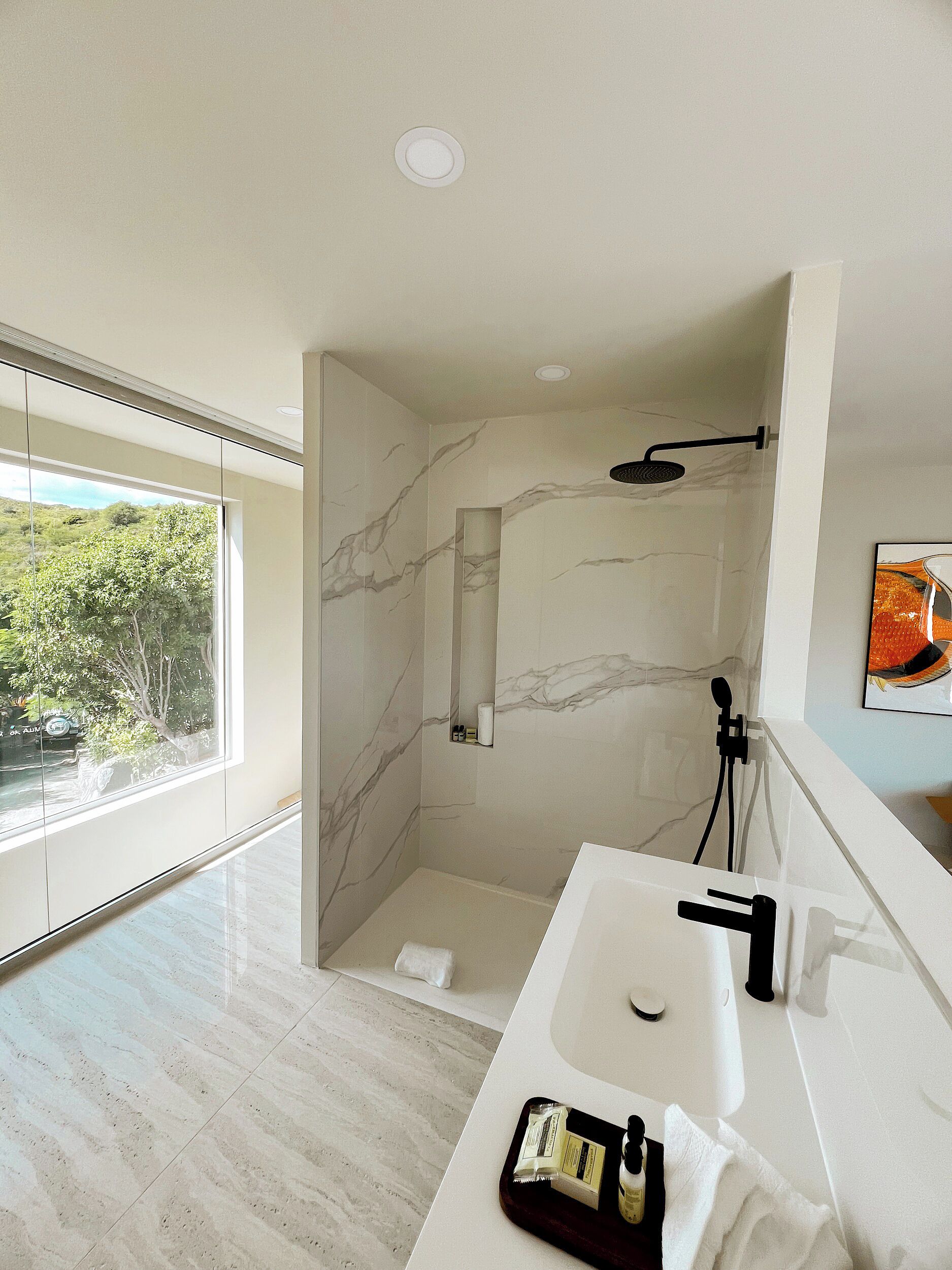 A modern bathroom with a large window, a shower, and a sink with toiletries.