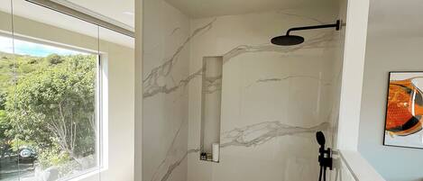 A modern bathroom with a large window, a shower, and a sink with toiletries.
