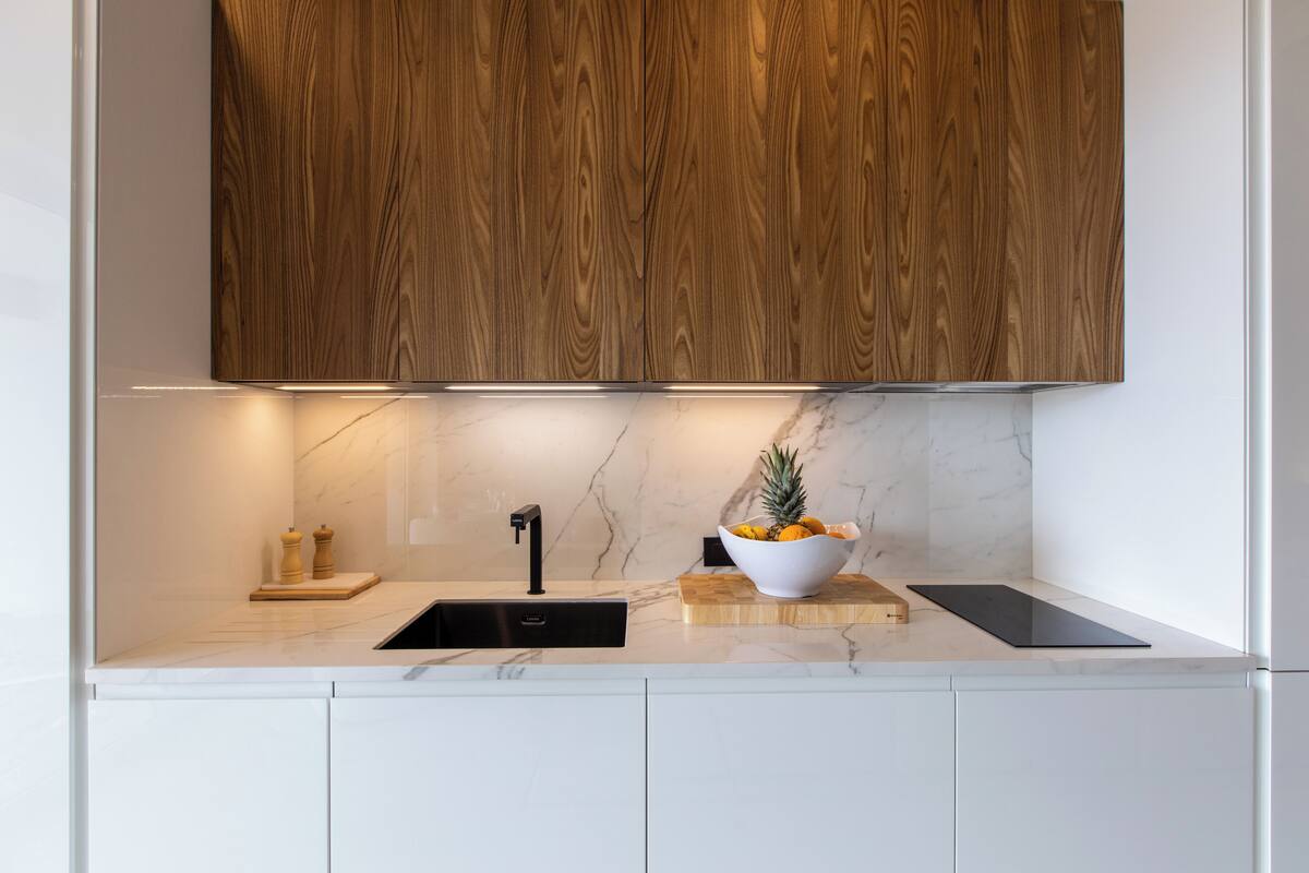 Une cuisine moderne avec des meubles en bois, un plan de travail en marbre, un évier noir et un saladier rempli de fruits.