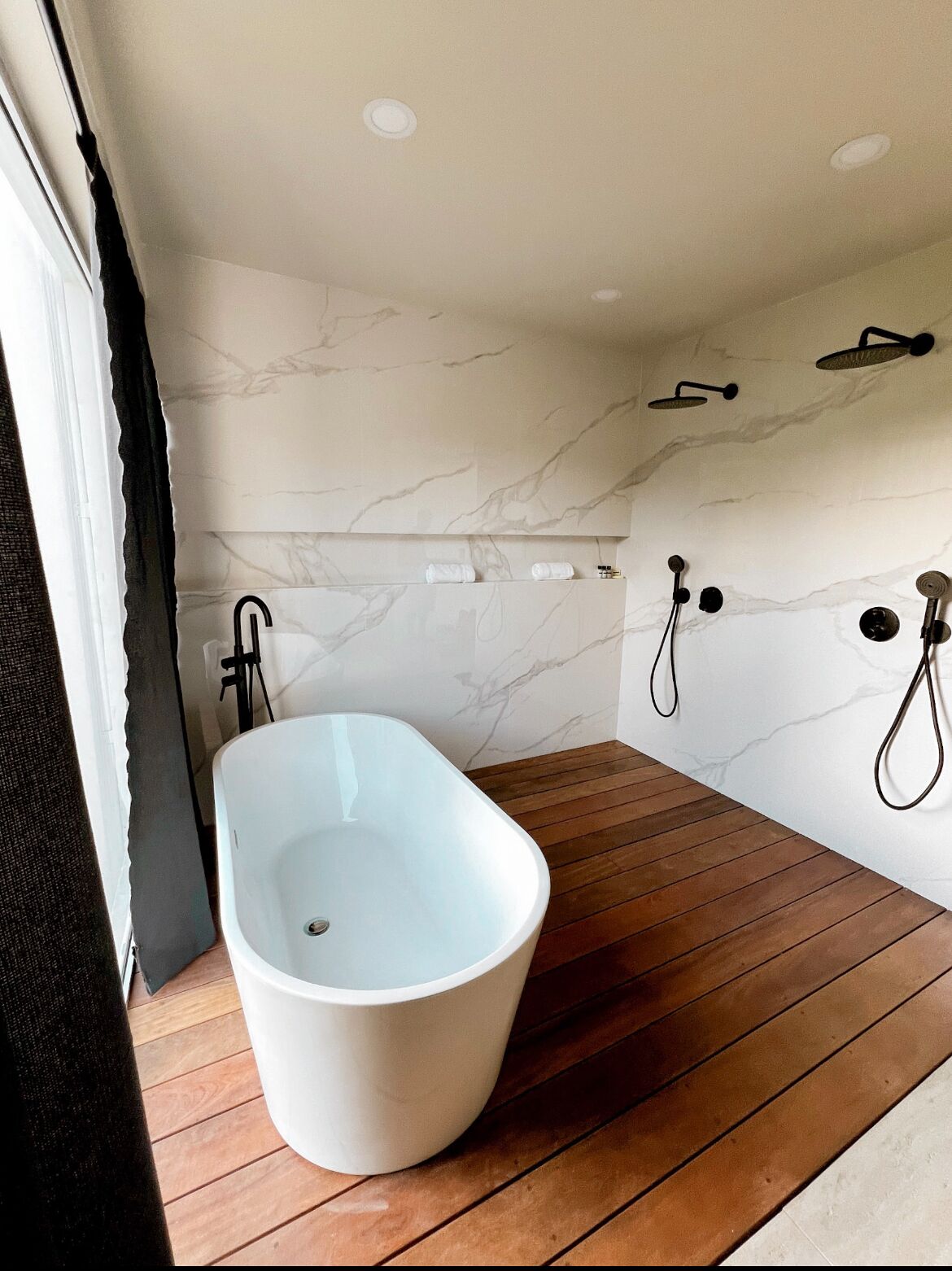 A modern bathroom with a freestanding bathtub, wooden flooring, and marble walls.