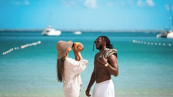 Un couple se tient sur une plage, d’où l’on a une vue dégagée sur l’océan et sur les bateaux qui se trouvent au loin.