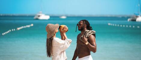 Una pareja está de pie en la playa con vista despejada al océano y barcos a lo lejos.