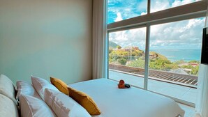 Un dormitorio con una cama grande, ropa de cama blanca y vistas al mar a través de un ventanal amplio.
