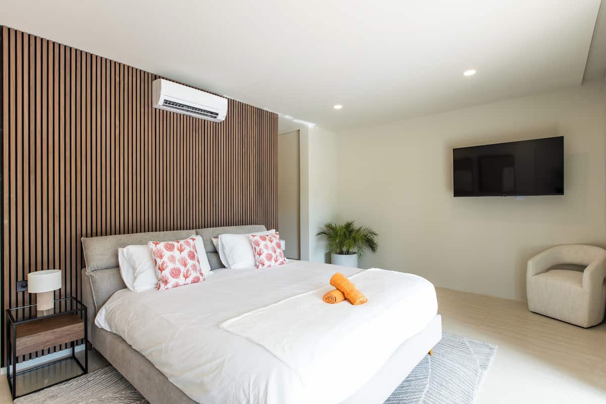 A modern bedroom with a large bed, a mounted TV, and a potted plant.