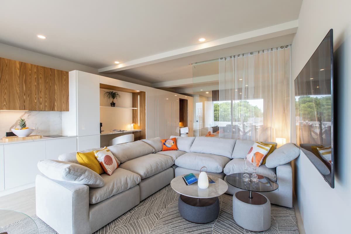 A modern living room with a sectional sofa, a round coffee table, and a kitchen area in the background.