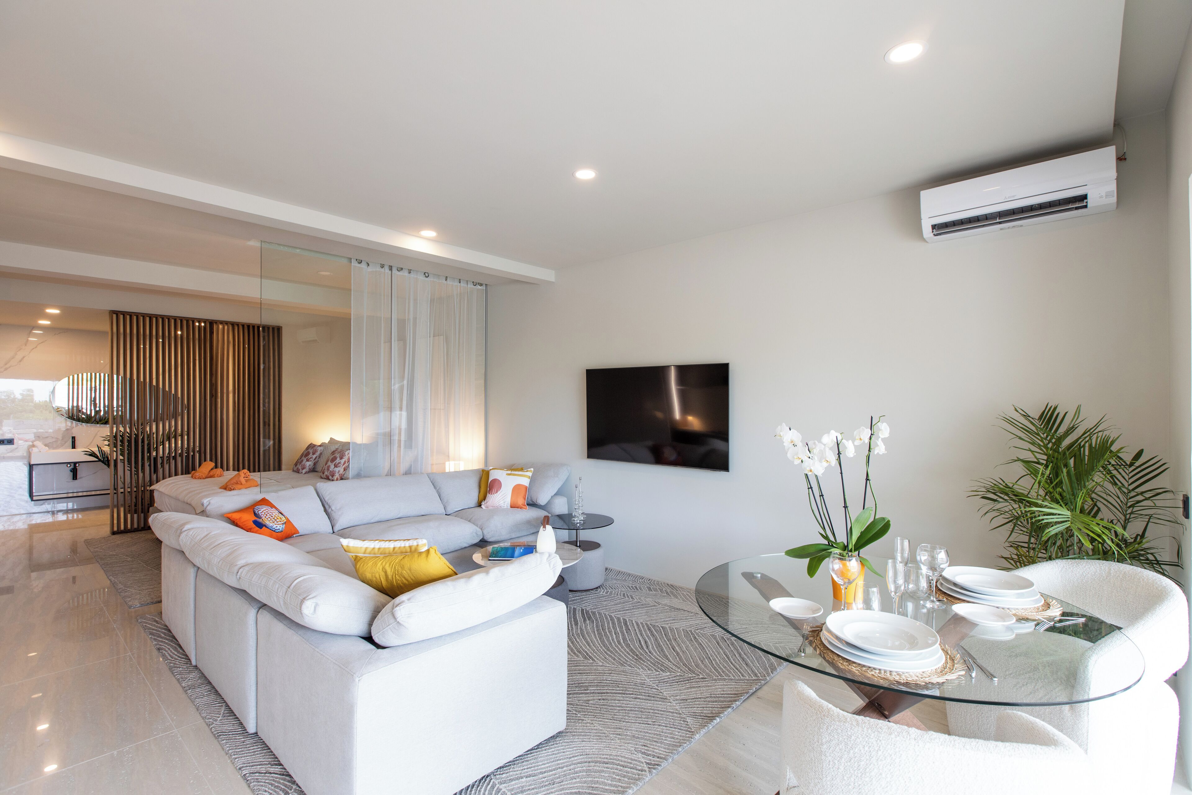A modern living room with a sofa, a glass coffee table, and a dining area with chairs and plates.