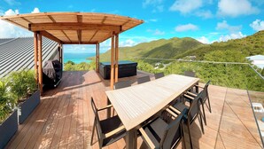 A wooden deck with a table and chairs, a covered seating area, and a hot tub. - Aura Anse-Marcel (Anse Marcel)