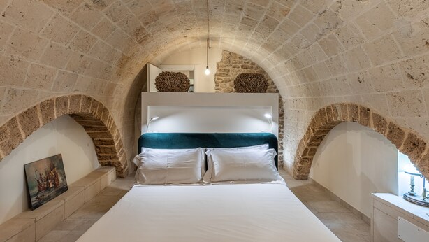 A bedroom with a stone arched ceiling, a bed with white linens, and a painting on the wall. - Palazzo Savino (Mesagne)