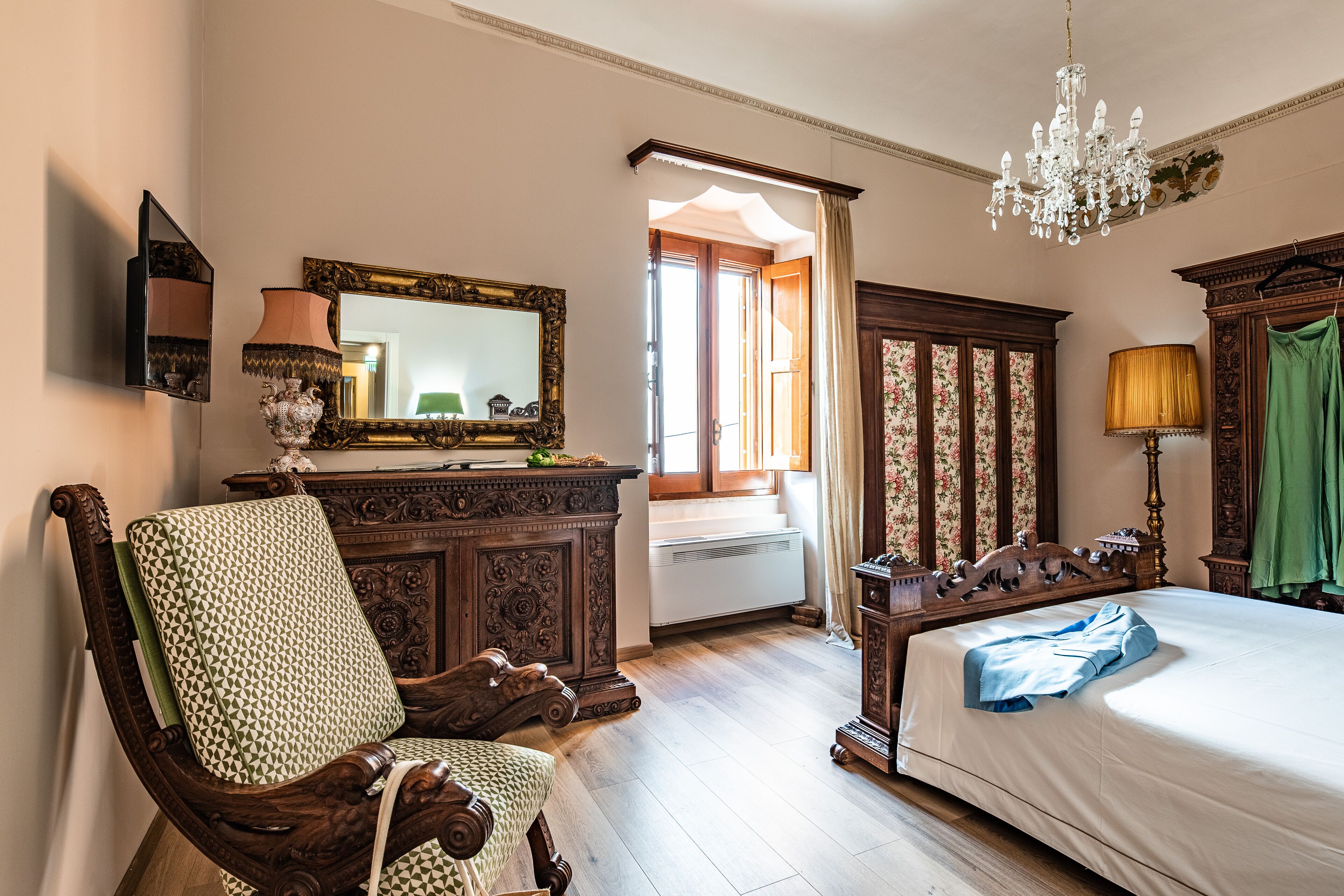 A traditional bedroom with a wooden bed, a large mirror, a chandelier, and a green curtain.