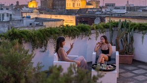 Two people seated on wicker chairs on a rooftop terrace with a cityscape in the background. - Palazzo Savino (Mesagne)