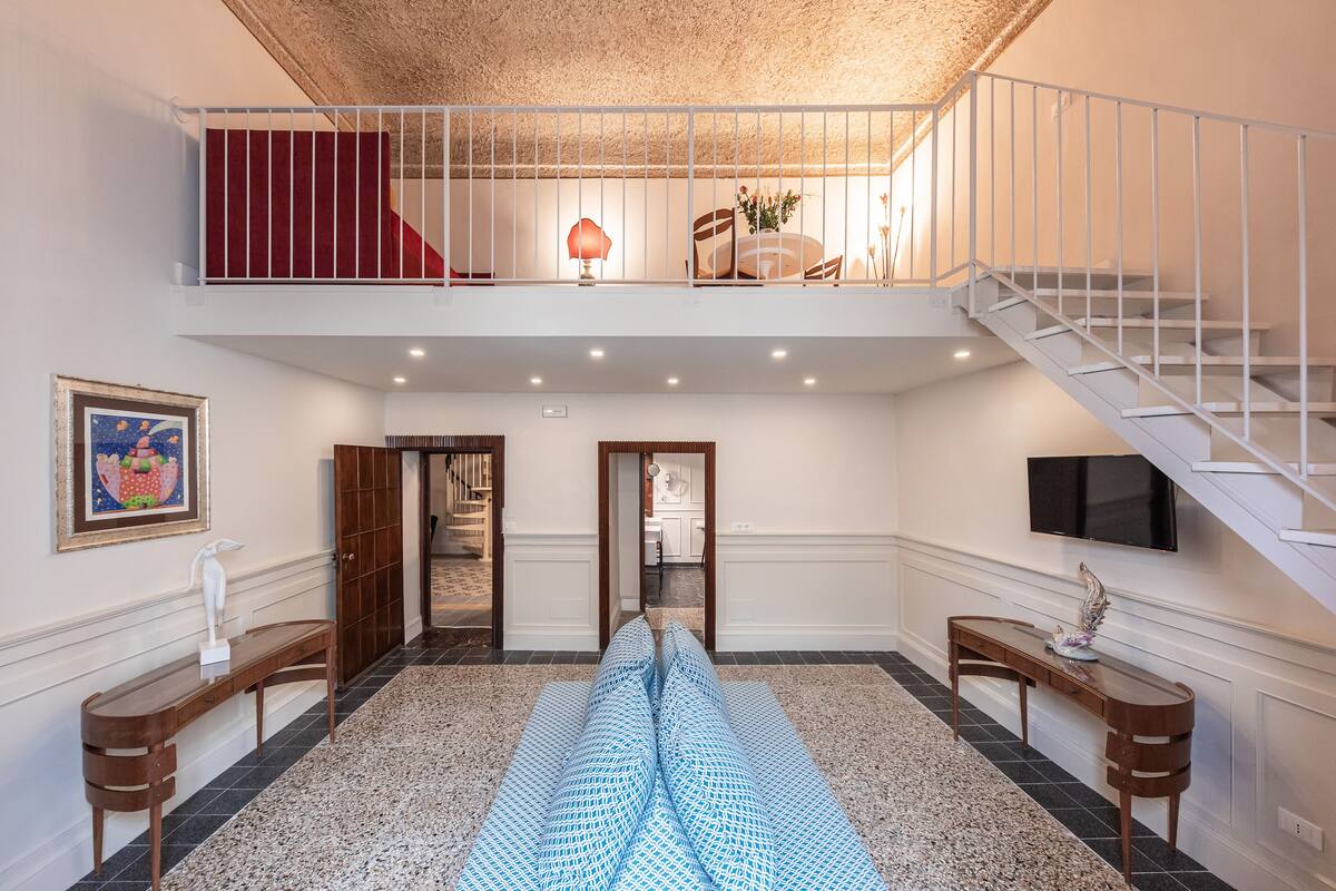 A spacious interior with a high ceiling, a staircase, and a view into a dining area.