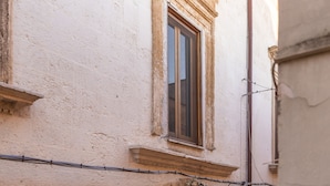 A narrow street with a stone archway leading to a wooden door, a window above, and a lamp post to the right. - Palazzo Savino (Mesagne)