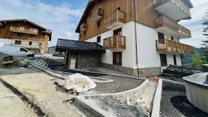 A multi-story building with wooden balconies, a stone foundation, and a paved driveway.