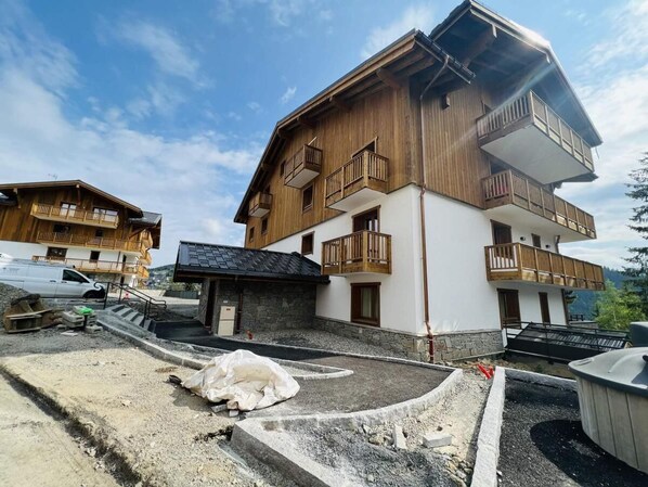 A multi-story building with wooden balconies, a stone foundation, and a paved driveway.